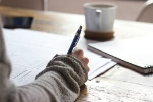 person-writing-on-brown-wooden-table-near-white-ceramic-mug-scaled-1